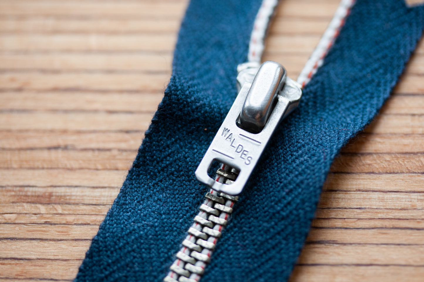 Z-002 Jeans-Reißverschluss aus Edelstahl – Waldes Schieber Nahaufnahme mit weiß-roter Webkante auf blauem Herringbone-Band