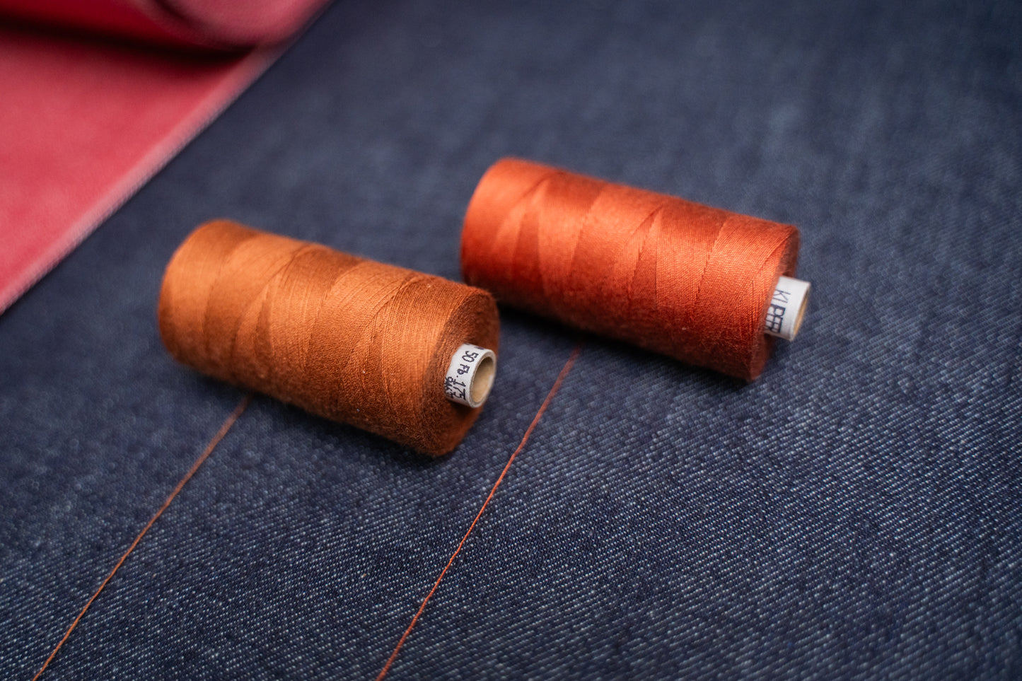 Jeans Starter Set 1 – Nahaufnahme der 2 kupferfarbenen Garnspulen auf hellem Indigo Selvage Denim